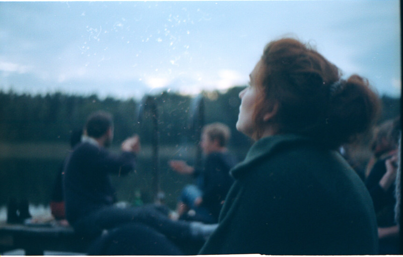 Red haired woman sits on the lake shore and looks to the sky.